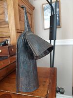 Side view of the very vintage iron double bell African Gankogui agogo instrument with tapered handle and two differently sized bells mounted one on top of the other.