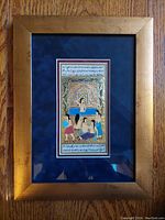 Full view of the framed foil artwork showing the Middle Eastern harem bath scene, set against a wood surface.