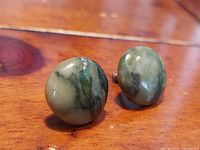Close-up front view of two round jadestone and sterling silver button earrings on a wooden surface.