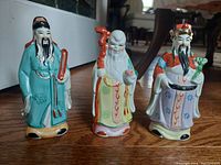 Front angled photo showing the three ceramic figurines standing in a row on a wooden floor, highlighting the details and colors of each.