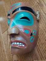 Side angle showing carved nose, teal and black painted eyes, and red and black markings on cheek.