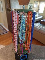 Front angled photo of the vintage green four-tiered necklace stand displaying multiple colorful bead necklaces hung on metal hooks.