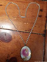 Photo of the entire necklace showing porcelain floral pendant on silver-tone chain on wooden surface.