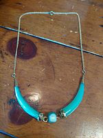 Photo of vintage Art Nouveau influenced necklace laid flat on wooden surface showing turquoise curved elements with gold-tone accents and central bead.