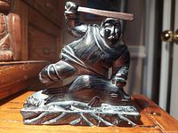 Front view of vintage Inuit hunter figurine with raised club poised to strike seal, sculpted from cultured stone