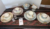 Front view of four sets of Bavaria gold-rimmed china including teacup, saucer, lunch plate, some with bread plates, cream pitcher, sugar bowl, and salt and pepper shakers on patterned cloth.
