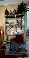 Full view of metal shelving unit with various Christmas decorations including artificial trees, nutcrackers, ornaments, and boxes of supplies.