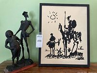 Photo showing the ceramic sculpture of Don Quixote and Sancho Panza alongside the framed Picasso sketch print.