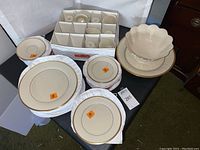Full set of Lenox china plates, cups, saucers, serving bowl and platter shown packed and arranged on table with storage covers.