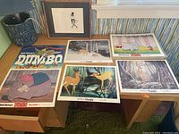 Seven Disney lithograph prints from Dumbo and Bambi laid out on table