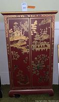 Front view of closed cabinet showing red-painted doors with gold chinoiserie landscape motifs and brass handles