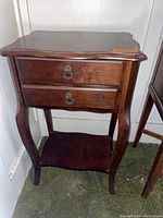 Wooden two drawer side table with curved legs and lower shelf, medium-dark brown finish, metal ring drawer pulls.