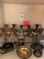 Front shelf view showing five pairs of candlesticks in silver-tone finish with red weight stickers.