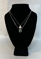 Front view of two sterling silver chains displayed on a black bust, showing the white pearl pendant on one chain and the green gemstone pendant on the other.