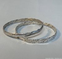 Two Mexican silver bangles lying side by side on a light surface, showing textured and rope design details clearly.