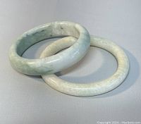 Two natural jade bangles placed side by side showing size difference and color variations.