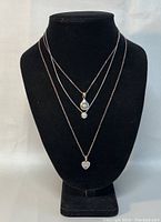 Front view of all three necklaces displayed on black bust, showing pendants for identification