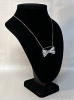Front view of the bow-shaped silver pendant on a black display bust.