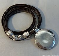 Full view of the dark brown leather multi-strand cord necklace with round sterling silver pendant and silver end caps