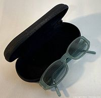 Open sunglasses case with the green-tinted rectangular sunglasses resting on the side.