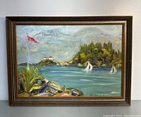 Frontal view of framed oil painting showing coastal landscape with flag, rocks, sailboats, trees, and buildings.