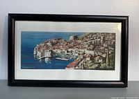 Framed rectangular artwork showing Dubrovnik city aerial view in color with black frame and white mat border.