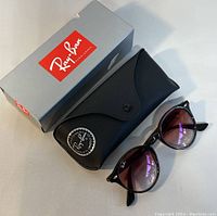Ray-Ban sunglasses next to their black leather original case and branded gray outer box on a white surface.