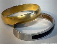 Two bracelets shown together: vintage Monet gold tone bangle and MCM stainless steel bangle with black inset.