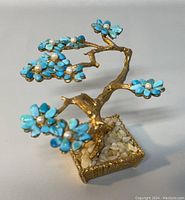 Front angle view of the bonsai tree sculpture showing turquoise jade petals with pearl centers and gold-tone branches.