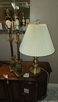 Two matching brass pineapple-themed table lamps without shades and a third gold-colored table lamp with white pleated shade on a wooden cabinet