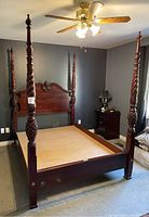 Full bed frame showing four twisted, pineapple-carved posts and a solid wood headboard with decorative scroll center.