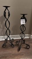 Pair of wrought iron candle holders with leaf design, showing front view on wooden floor.