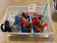 Plastic bin containing multiple clamps and accessories, including small clamps with red handles, and assorted items.