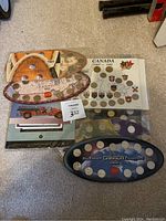 Four coin displays laid out on floor, including Canada 1867-1992 coins, millennium 2000 coin set, 1999 coin set, and a provincial quarter collection and coin information sheet.