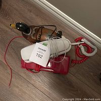 Lot of three phones stacked on the floor showing the duck phone on top and red car phone underneath with the white phone on top wrapped in cord.