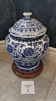 Front view of ginger jar showing blue floral patterns and lid with knob handle on wooden base.