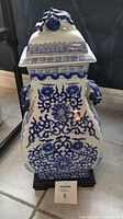 Front view of the vintage blue and white chinoiserie ginger jar with lidded top and ornate side handles, mounted on a wooden base