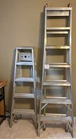 Two aluminum step ladders side by side showing different sizes, both in upright position.