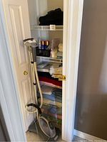 Shark fabric steamer and various linens like towels and blankets on shelves inside a closet