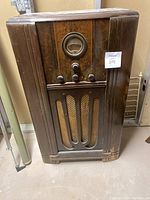 Front view of vintage Philco floor radio showing wood cabinet with scratches, control knobs, radio dial, and speaker grille.