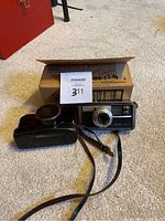 Kodak Instamatic 500 camera, black leather case, and Canon lens accessory with box on carpet.