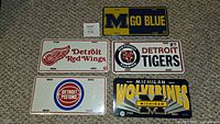 Five decorative license plates representing sports teams from Michigan, arranged on carpet