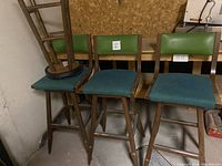 Three green stools with blue cushioned seats and green vinyl backrests shown next to each other in basement storage area