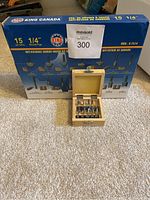 Box with King Canada anti-kickback carbide router bit set and wooden bit case in front on carpet.