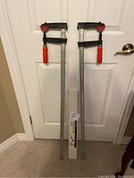 Front view of two 4-way speed frame clamps standing side by side against a white door.