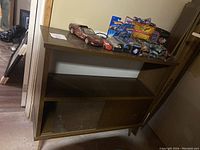 Wooden brown cabinet with shelves and doors, showing toy cars and collectibles on top shelf.