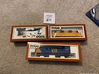 Three TYCO model train cars in original packaging: a yellow Union Pacific gondola car, a blue VIA train engine, and a CN VIA caboose.