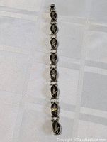 Full view of vintage sterling silver bracelet with multiple linked oval sections featuring figure inlays on a white fabric background.