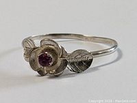 Side view of sterling silver ring showcasing the carved flower with a central ruby stone and detailed leaves on either side.