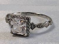 Front angled close-up showing the square crystal quartz stone set in sterling silver with ornate band details and smaller surrounding stones.